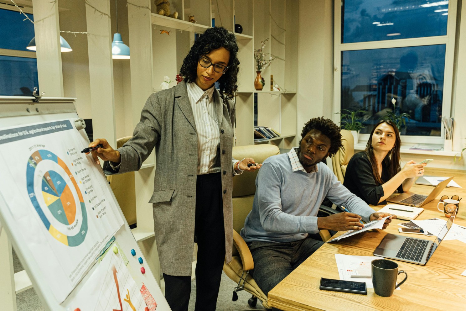 A woman presenting from a flipchart in a cluttered boardroom