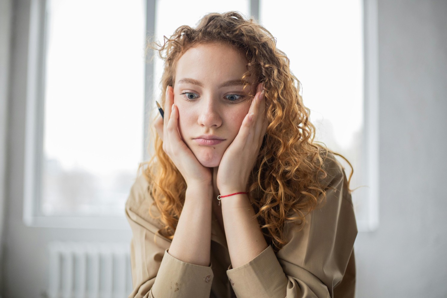 A woman with curly hair sitting with her head in her hands, holding a pen in one of them