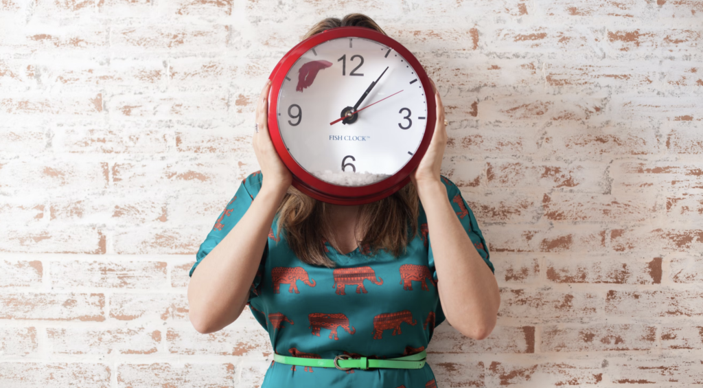 woman in a patterned dress holding up a red clock in front of her face