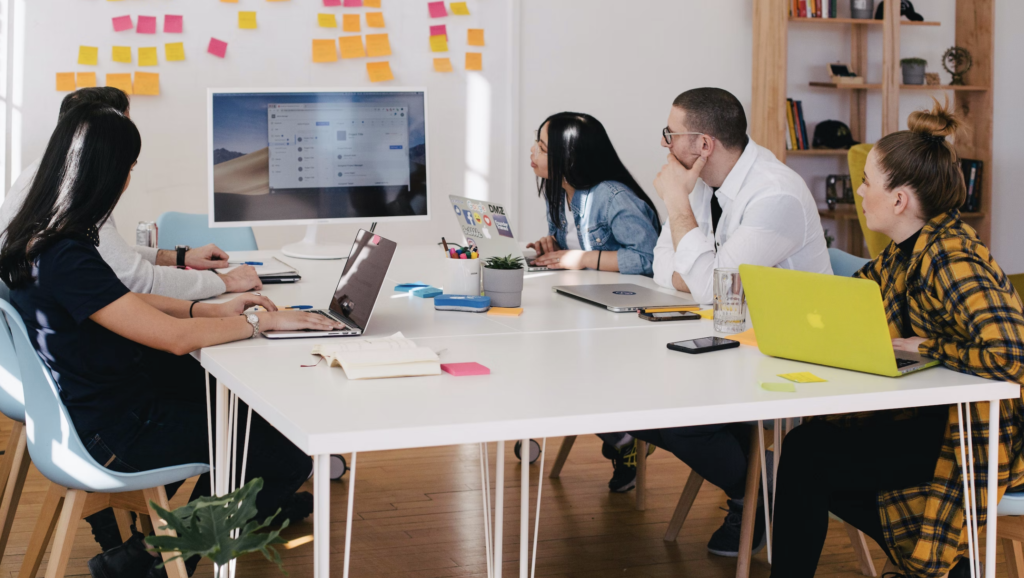 a group of co-workers sat around a desk and watching a presentation 