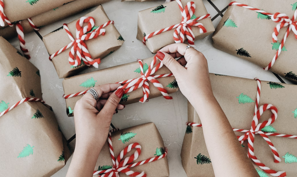 a pair of hands tying the final ribbon a set of brown paper wrapped christmas gifts.