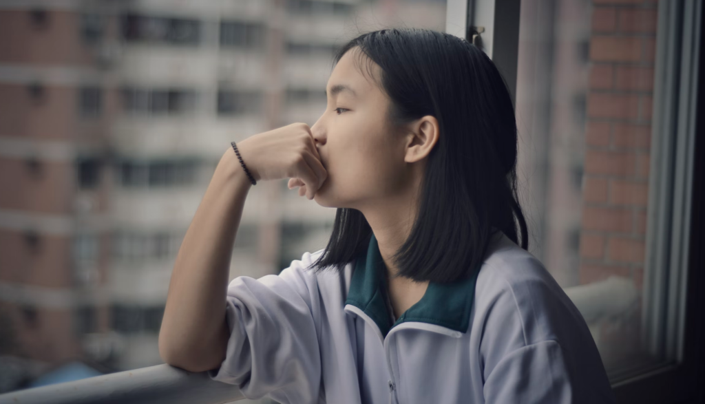 a child with short black hair looking out of a window 
