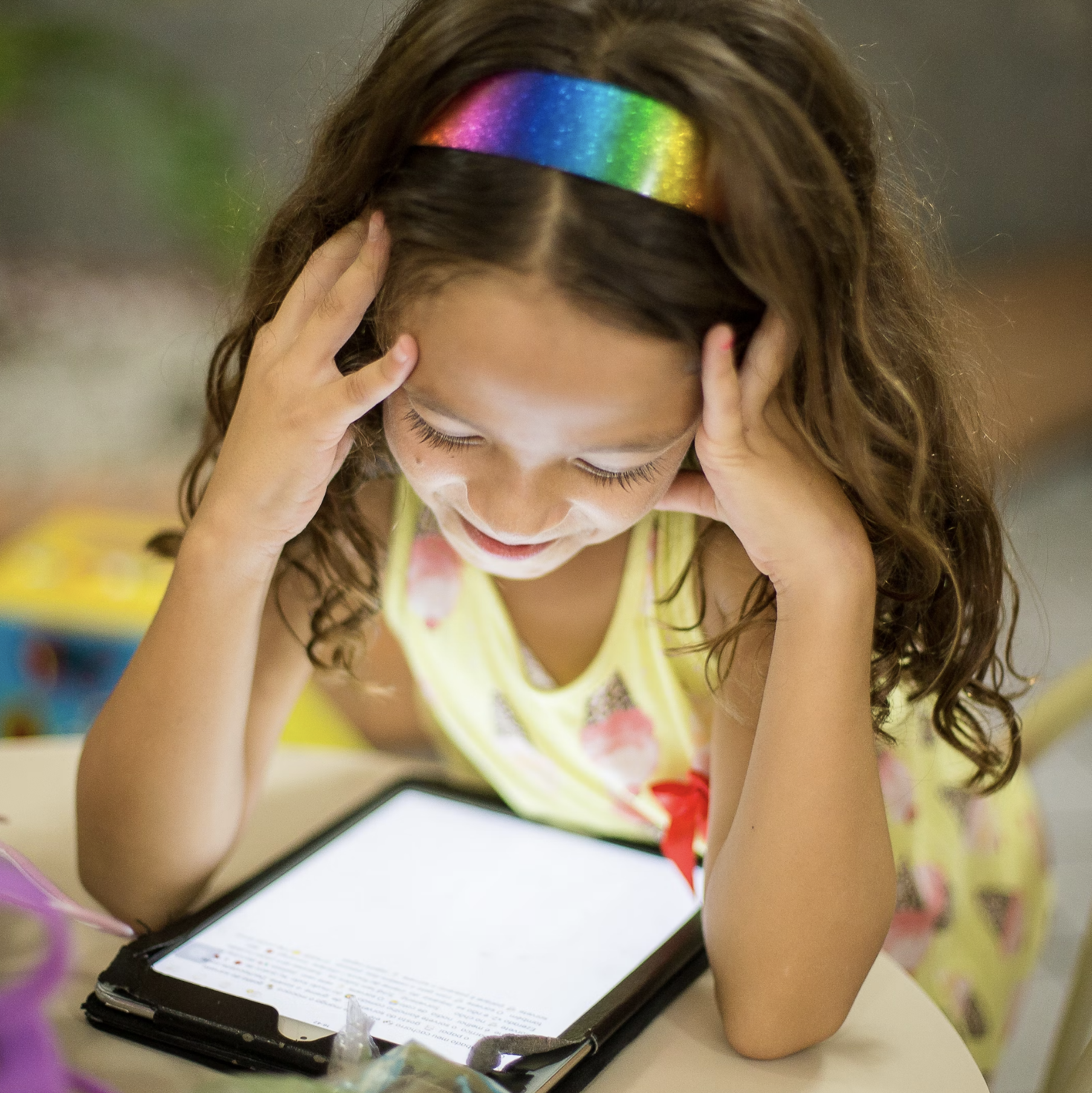 young child in a headband looking happily down at an iPad