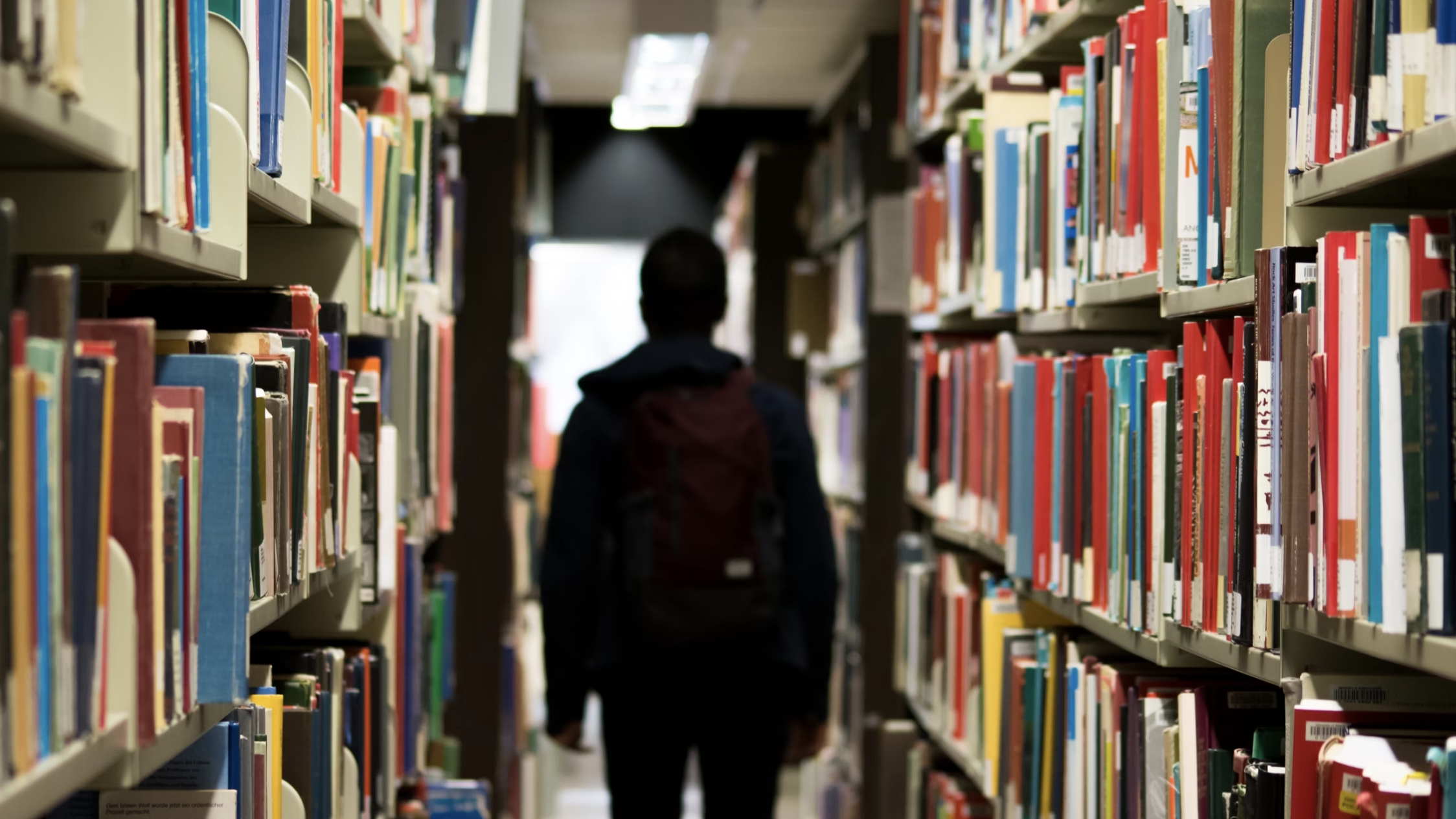 a silhouette of a figure walking between library shelves, carrying a backpack