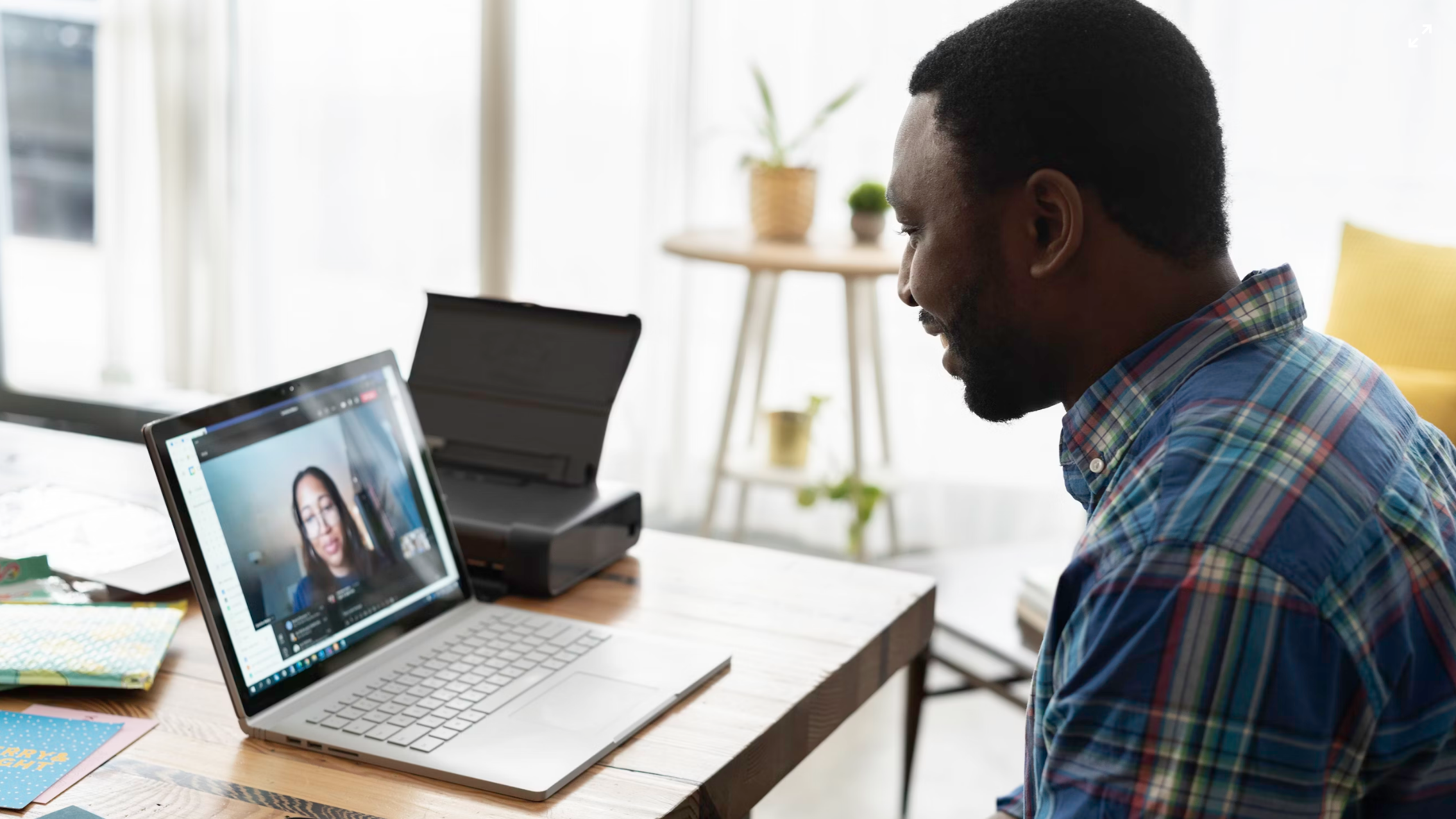 a smiling man in a plaid shirt sat at a laptop, talking to a woman on a video call