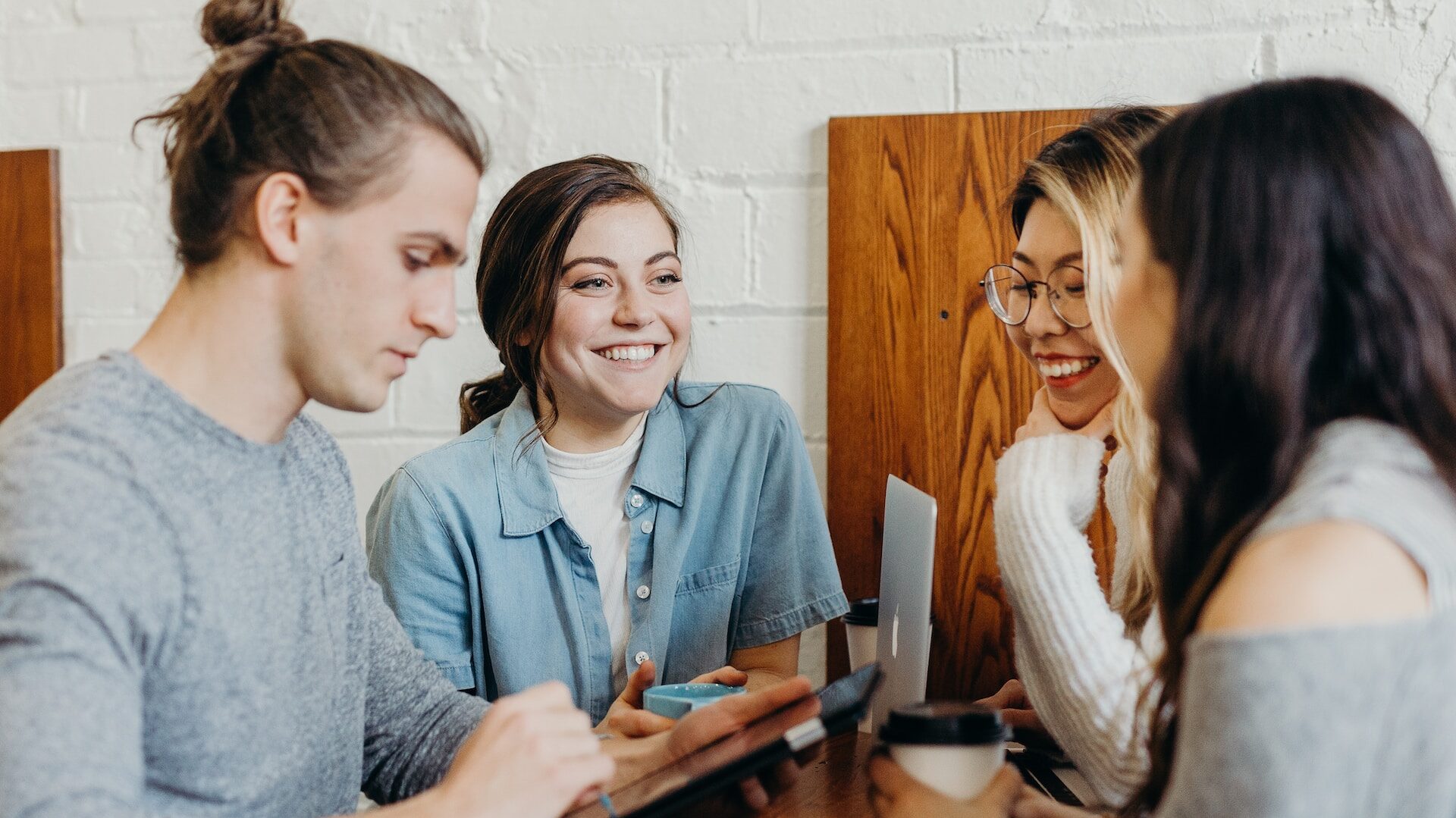 a group of young workers dressed casually, sat around a screen and drinking coffee 