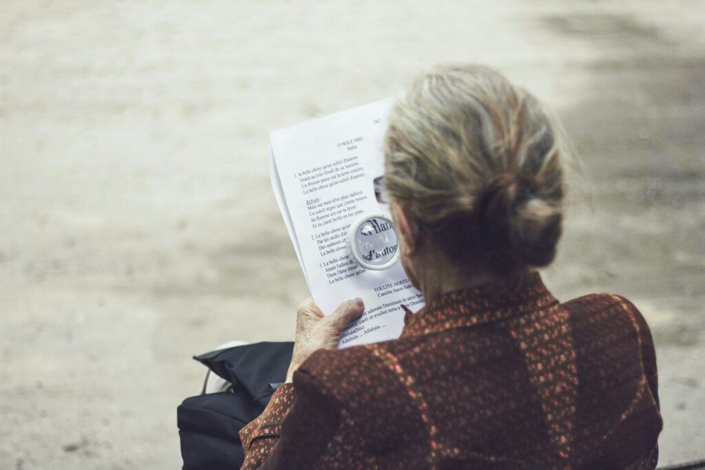 a person with long grey hair in a bun reading a magazine with a magnifying glass