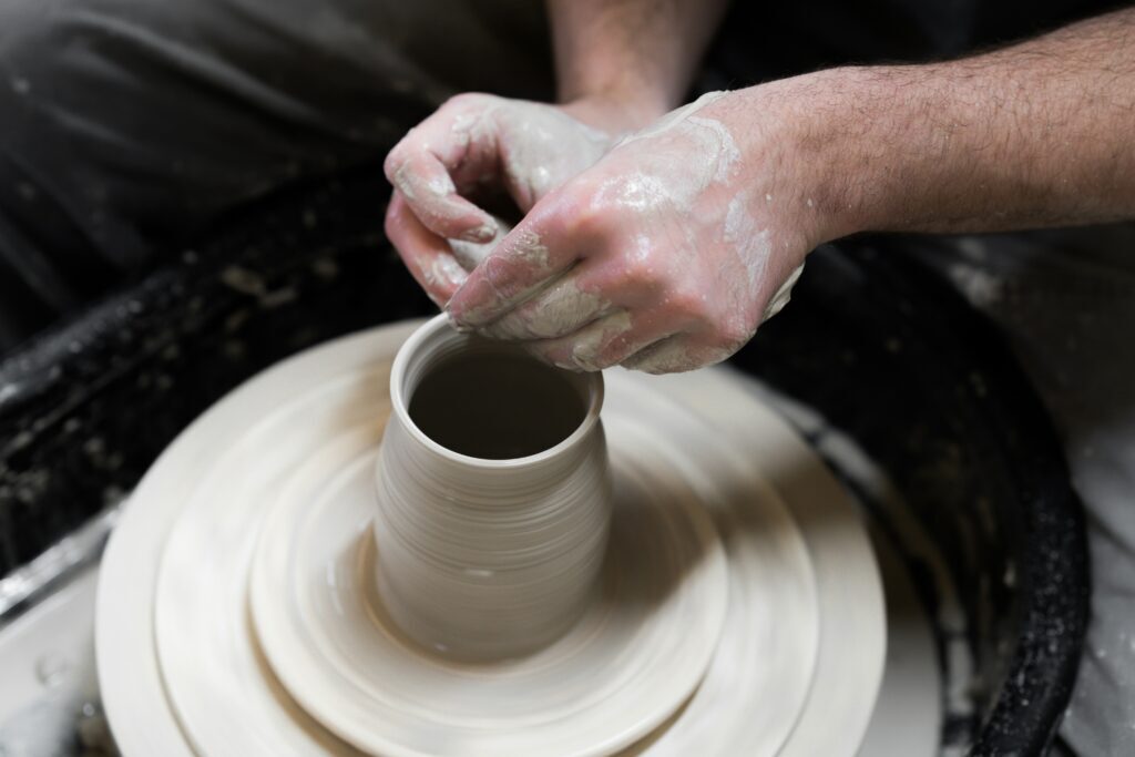 Hands throwing a small clay pot on a wheel