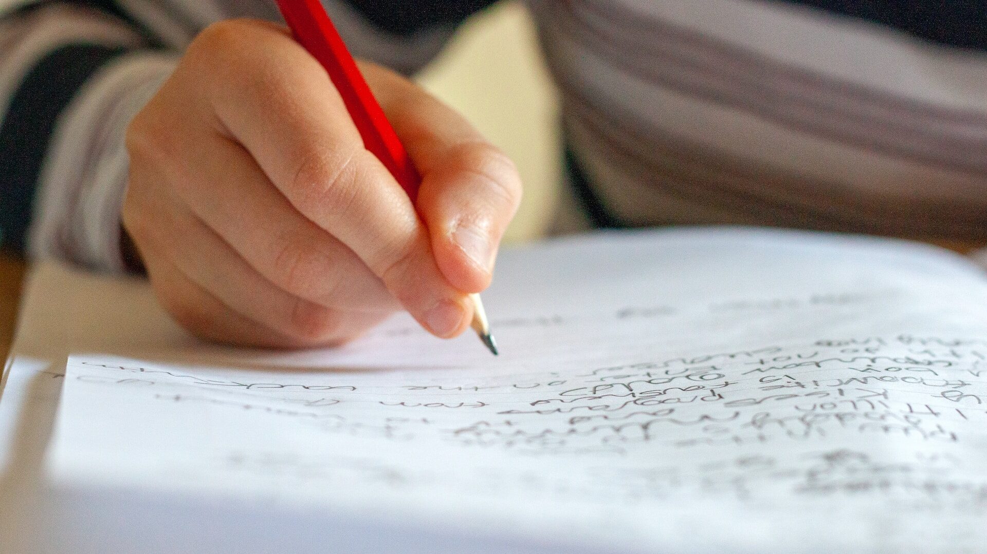 the dysgraphia guide: a child's hand holding a red pencil above a lined page half-filled with handwriting. 