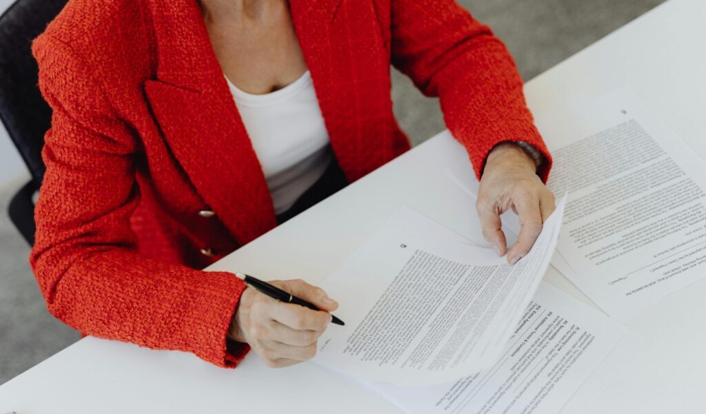 A person in a smart red suit holding a resume in their hands, a pen poised to make an edit