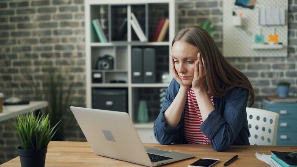 Woman with her head in her hands, looking at a laptop screen.