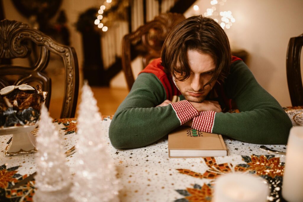 A person with their fringe over their face, looking upset, slumped over a festive dining table