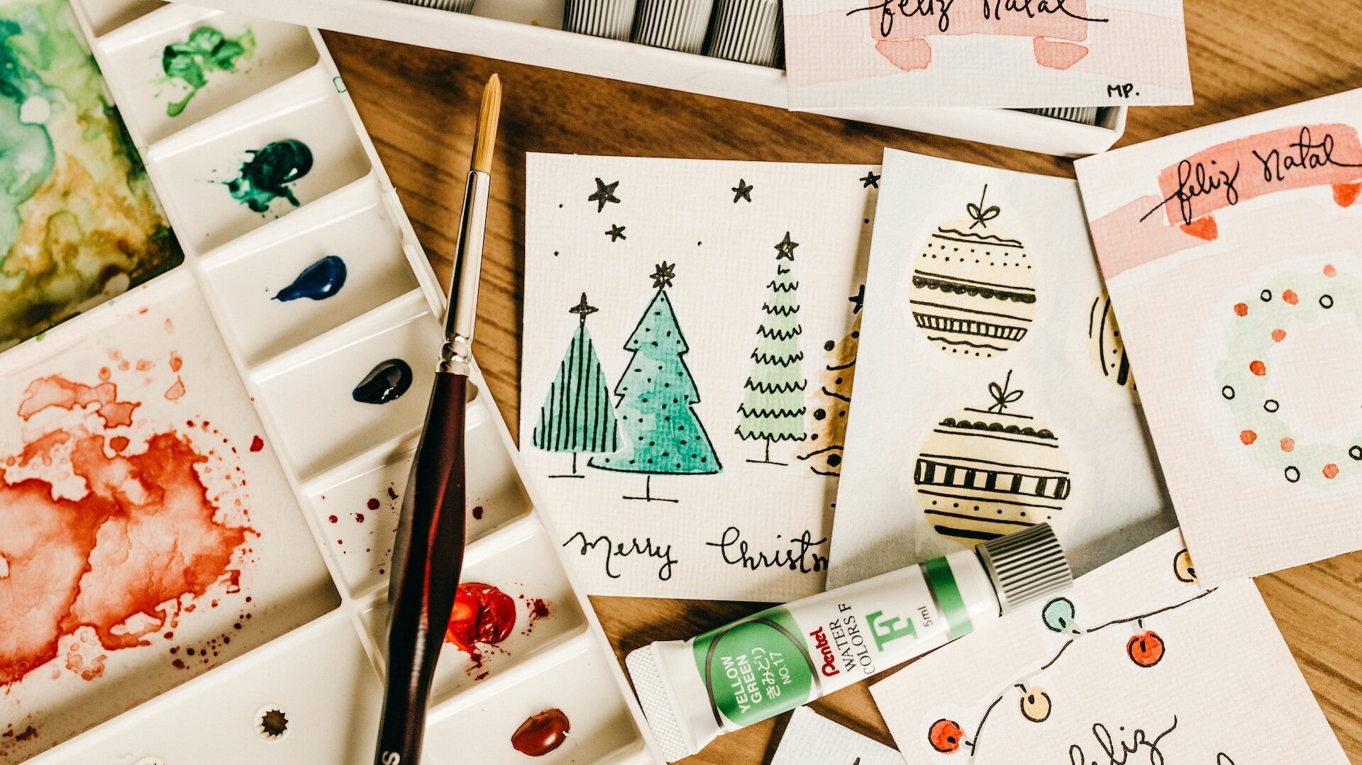 hand-painted christmas cards, a watercolour palette, and a paintbrush 