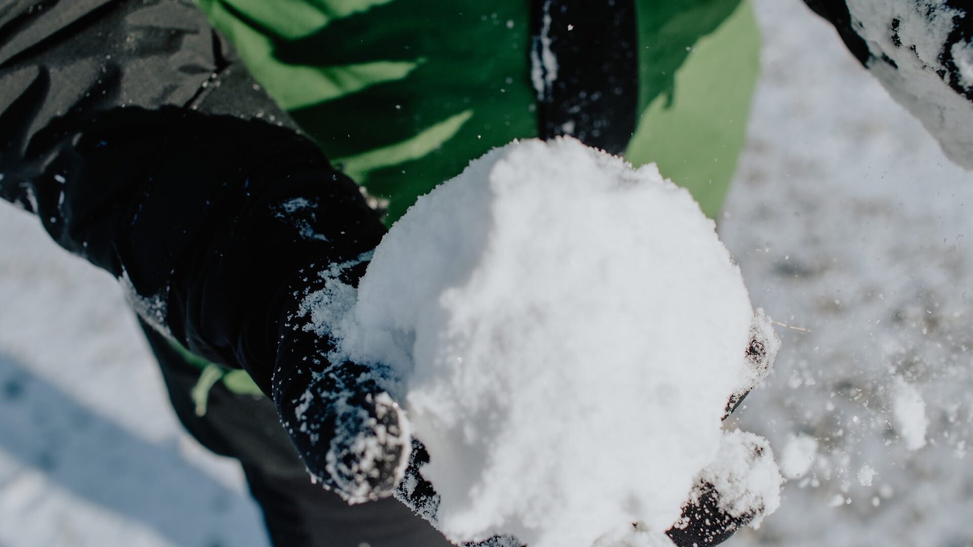 gloved hands holding a snowball against a snowy backdrop 