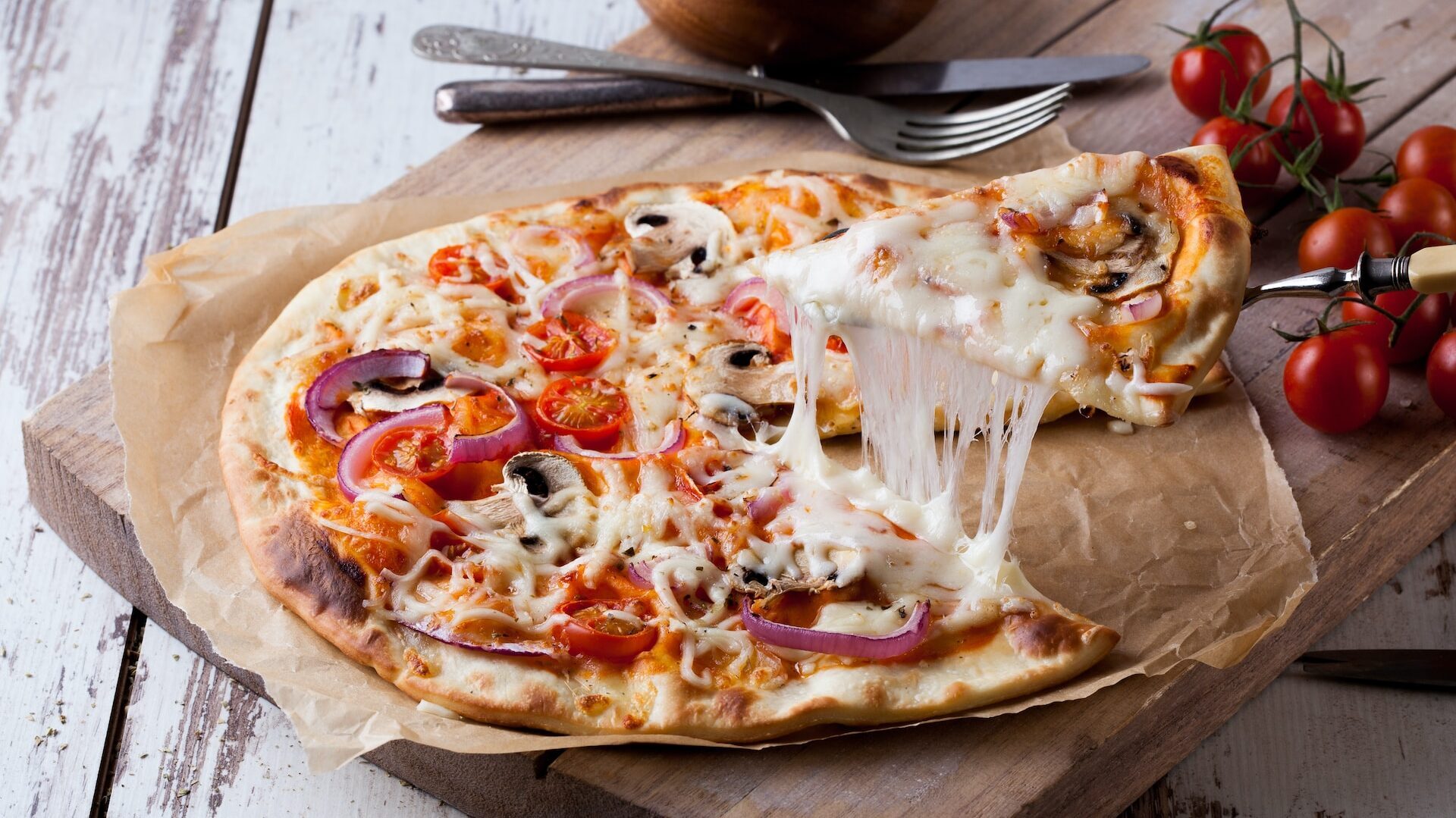 dyslexia and cooking: a cheese pull photograph from a mushroom and onion pizza, with fresh tomatoes on a wooden chopping board close by. 
