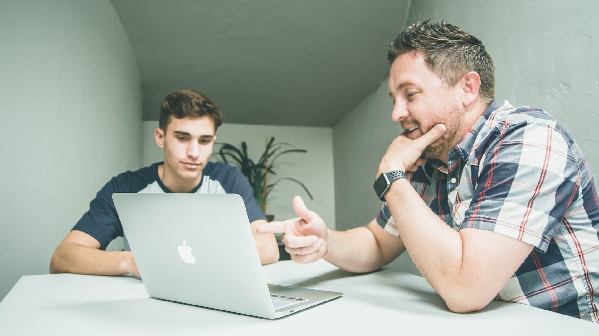 two people conversing in front of an open macbook. Both look interested and happy. 
