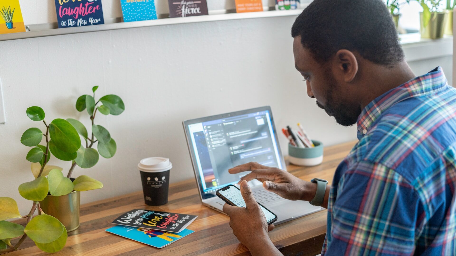 a man with dyslexia at work, using an iphone. he's got an open laptop and a coffee on the table in front of him.