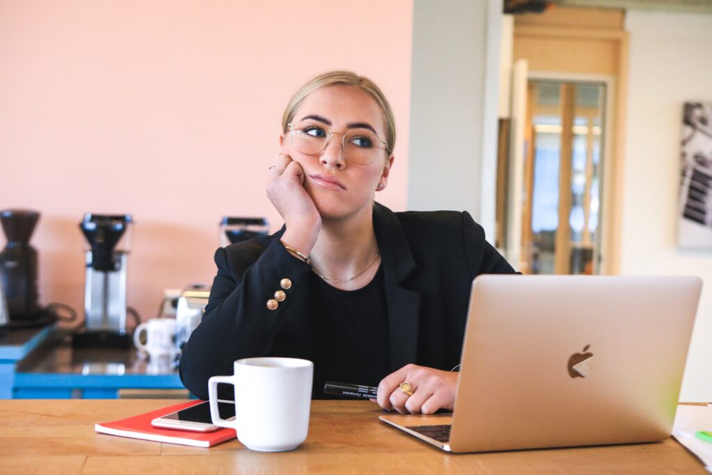 woman in a blazer looking bored in front of a macbook 