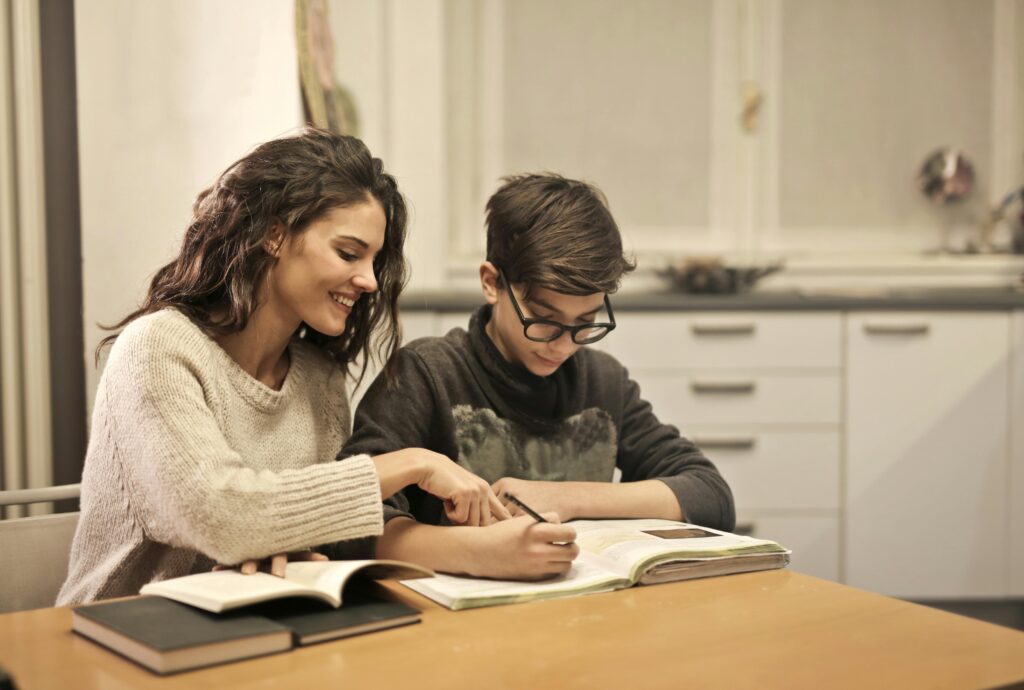 Woman supporting a young student with homework at the kitchen table 