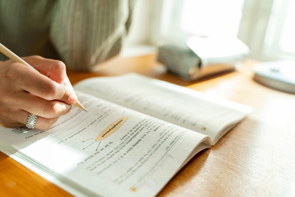 Hand wearing a wring holding a pencil, poised above a textbook