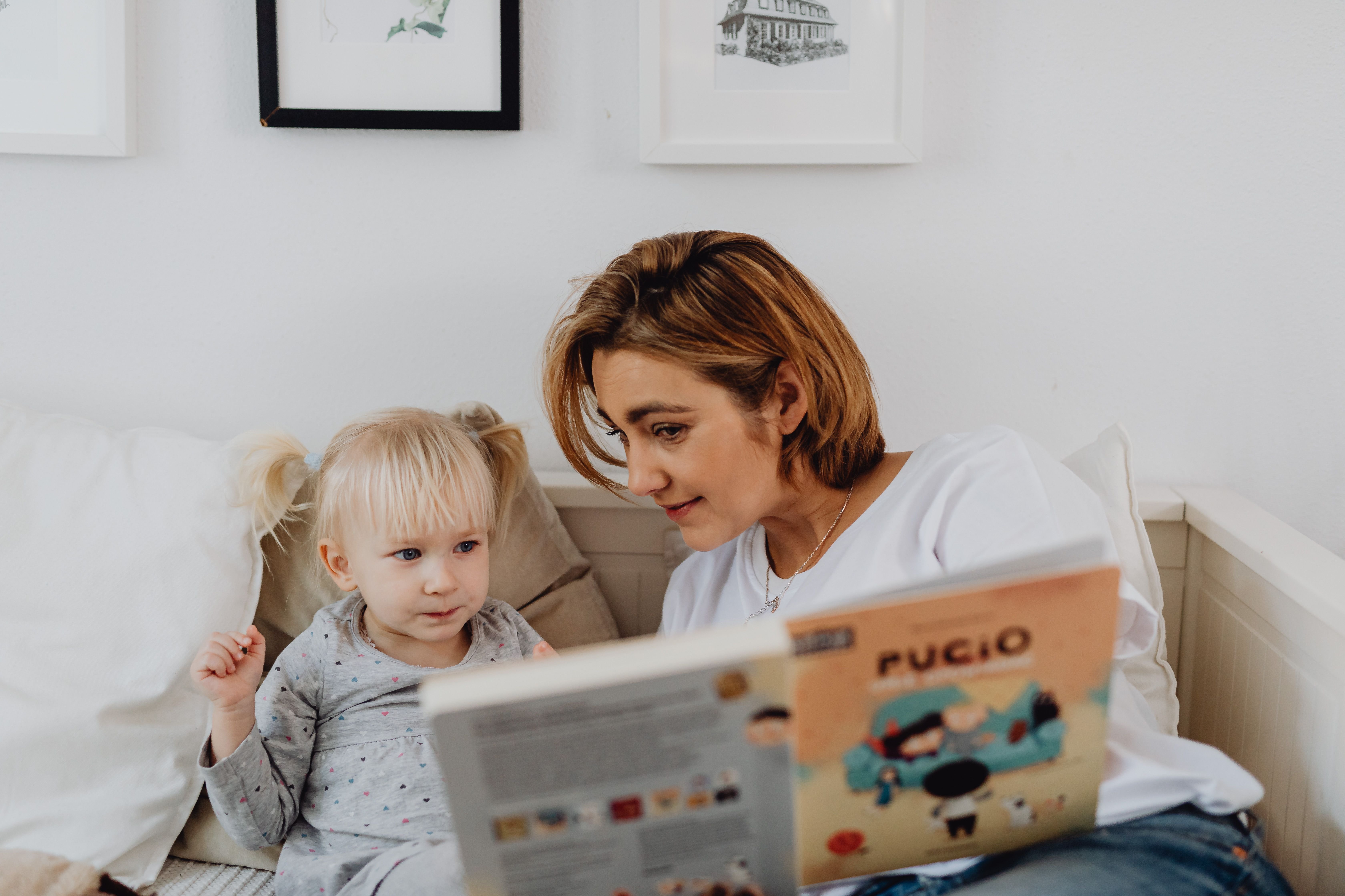 lady reading a book to a little girl sat on the sofa