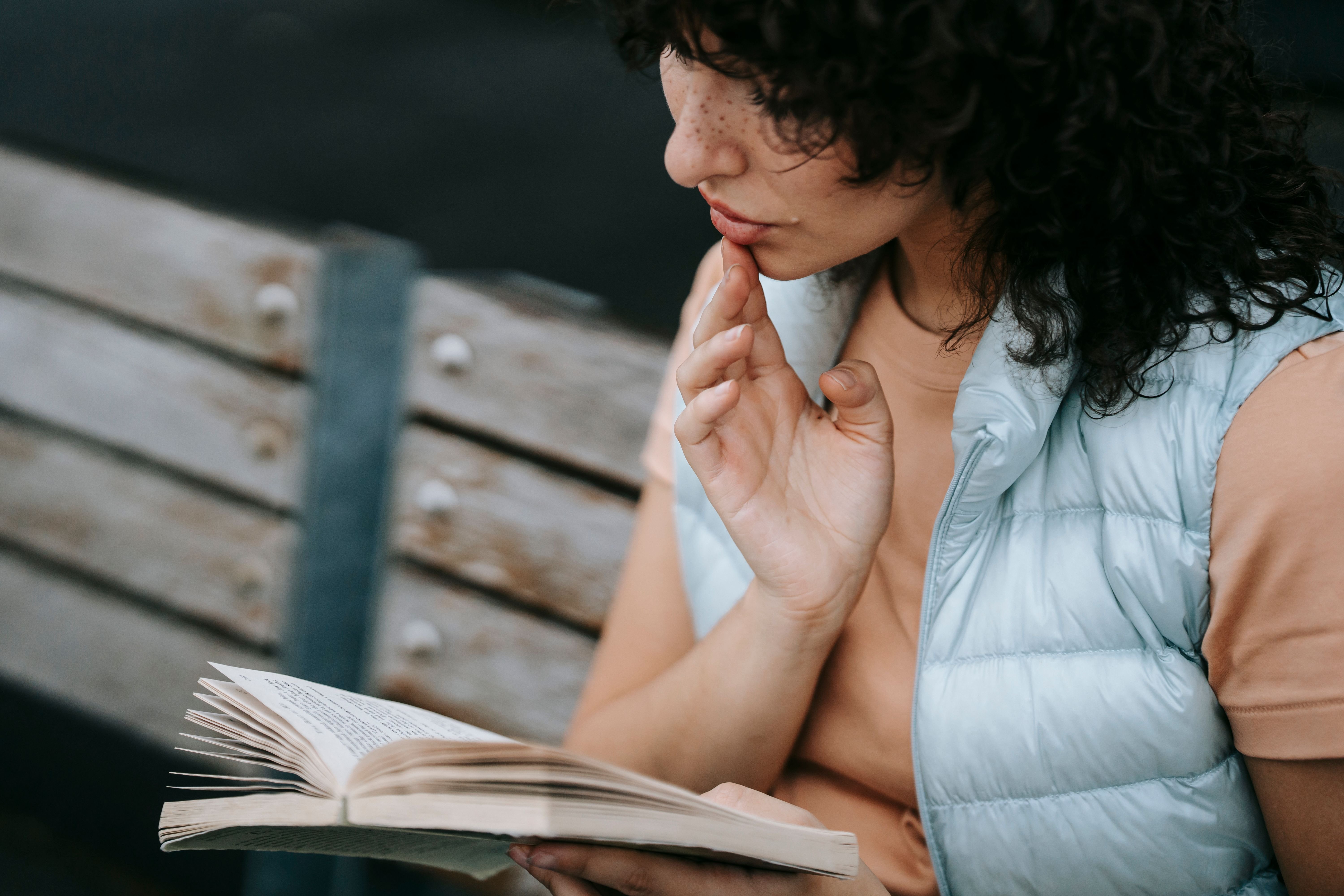 woman sat on a wooden bench reading a book