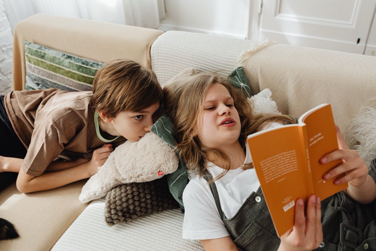 two children reading a book on the sofa
