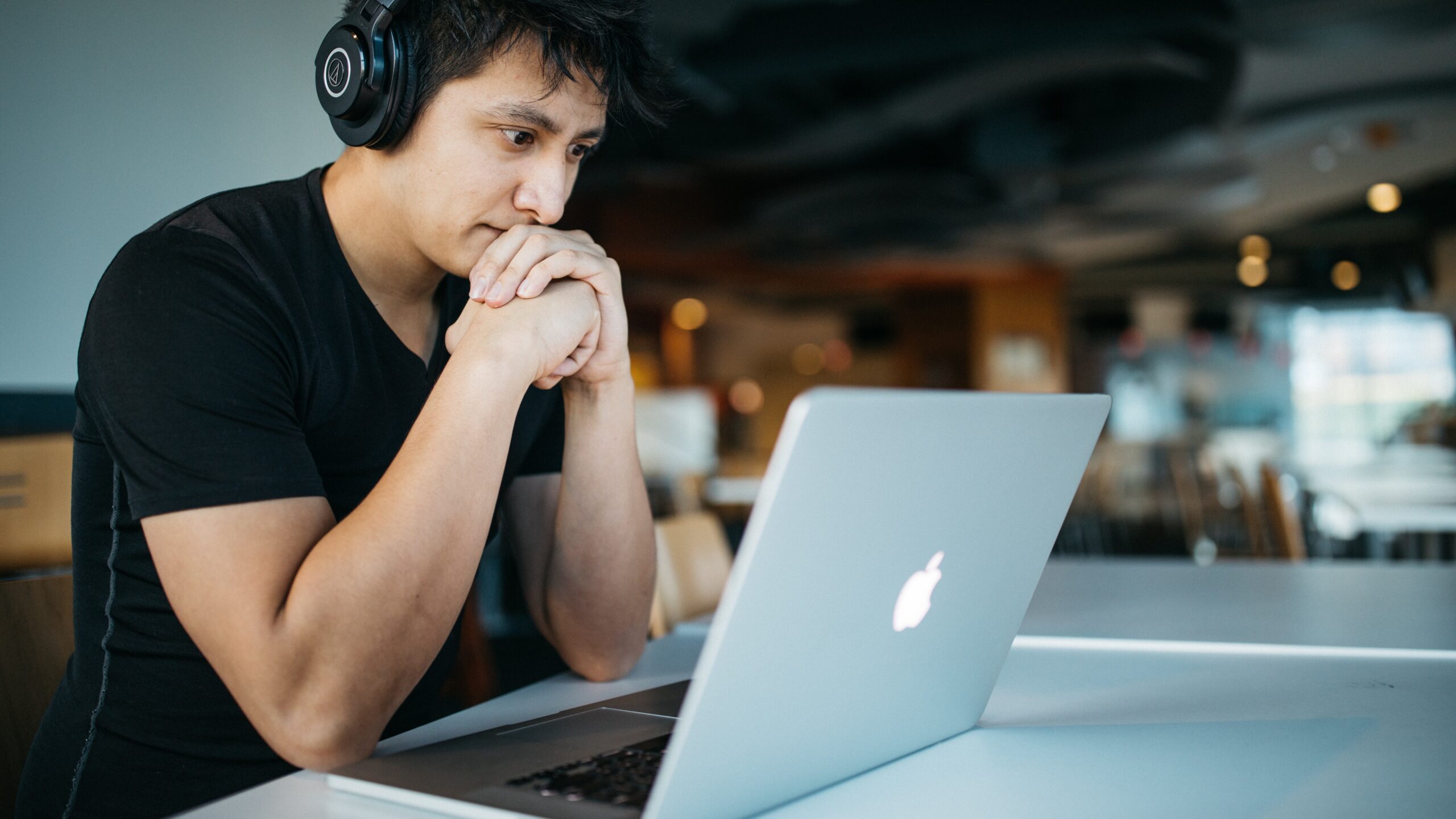 man in headphones looking worried in front of a macbook